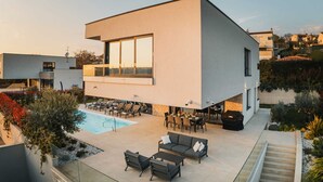 Une maison moderne à deux étages, dotée d’une piscine, d’un espace de détente extérieur et offrant une vue sur le quartier environnant.