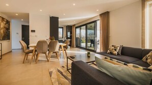 Un salon moderne comprenant un canapé, une table à manger avec des chaises et une grande porte-fenêtre coulissante donnant sur un balcon.