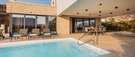 A modern outdoor pool area with lounge chairs and a barbecue setup.