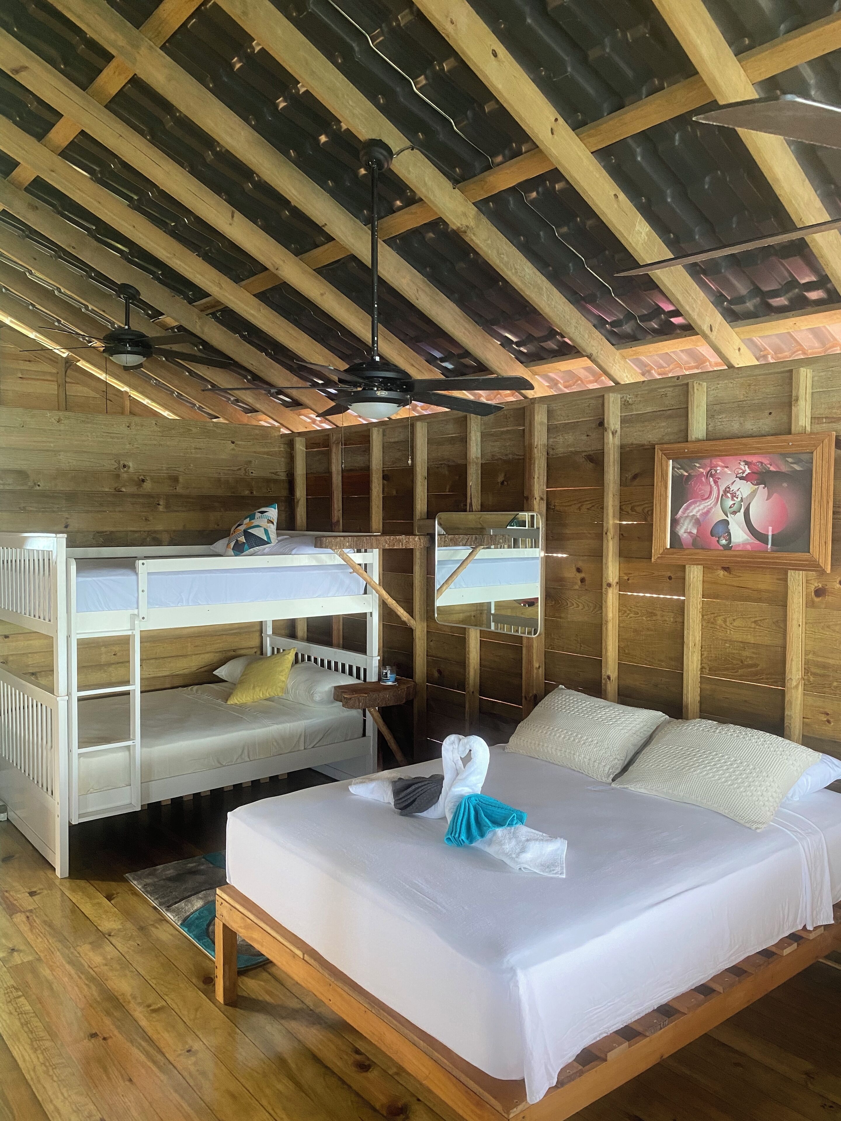 A wooden cabin-style room with bunk beds, a single bed, a ceiling fan, and a framed picture on the wall.