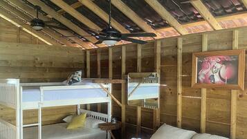 A wooden cabin-style room with bunk beds, a single bed, a ceiling fan, and a framed picture on the wall.