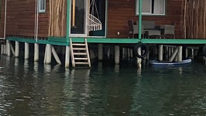 Una casa a due piani in legno con tetto verde, posata su palafitte sull'acqua.