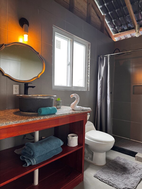 Une salle de bain avec un meuble-lavabo en bois, un miroir, un lavabo, des toilettes, une douche et une fenêtre.