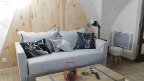 Un salon moderne avec un canapé blanc, des coussins à motifs, une table basse en bois et un téléviseur posé sur un meuble.