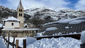 Un village enneigé, avec un clocher d’église, des clôtures en bois et des toits couverts de neige.