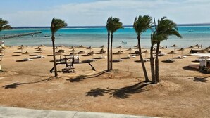 Una playa con palmeras, sombrillas y sillas de descanso.