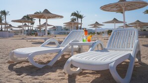 Dos sillones blancos con una mesita entre ellos, una bebida y varias sombrillas de playa al fondo.