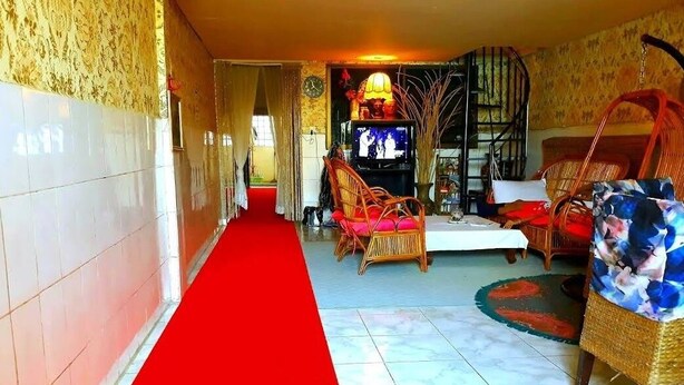 A hallway with a red carpet leading to a seating area with wicker furniture and a television.