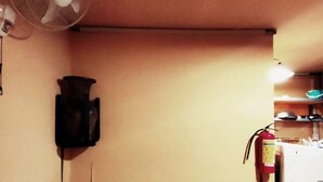 A room with a ceiling fan, a fire extinguisher, and a small table with a lamp.
