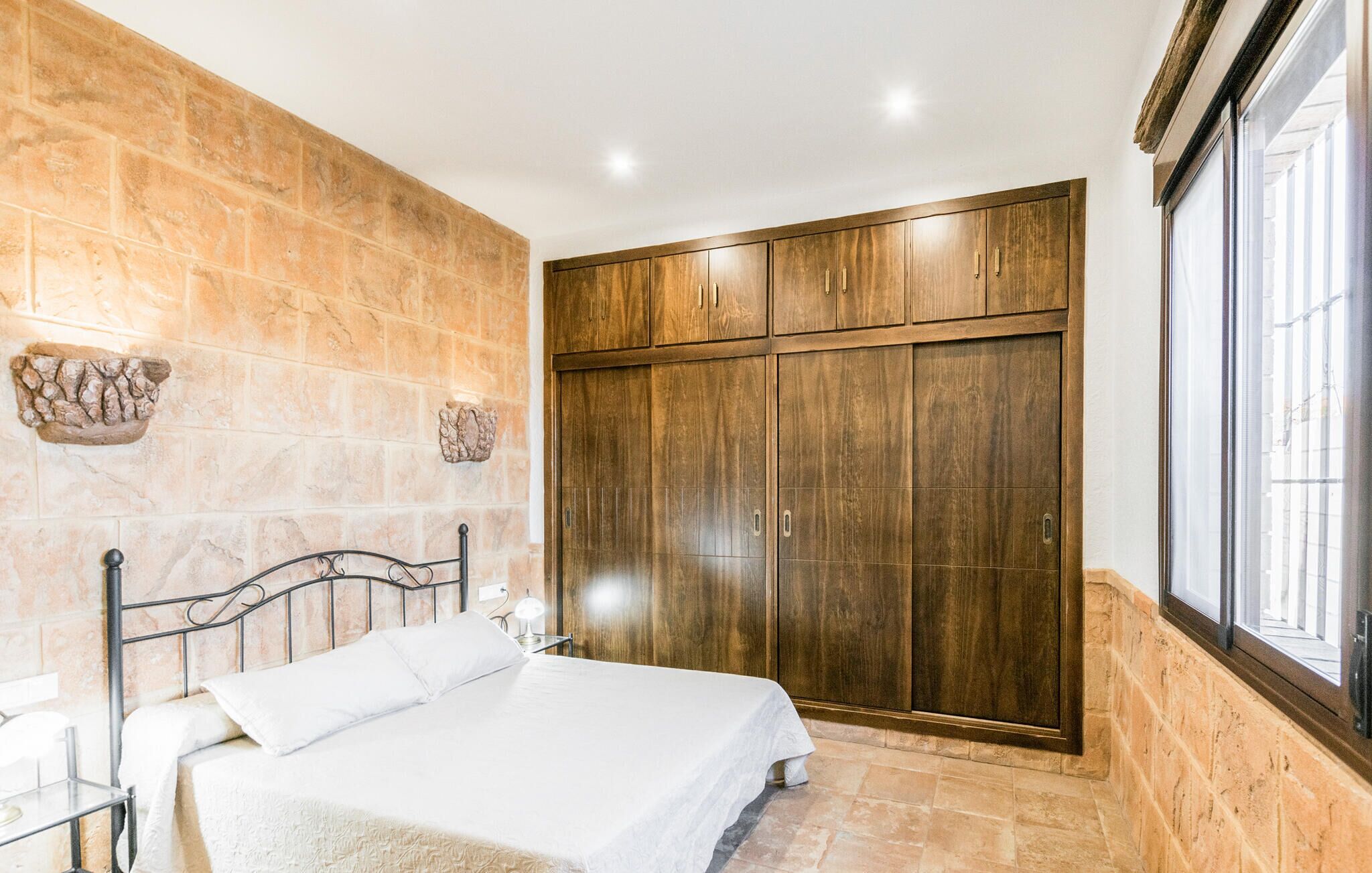 Un dormitorio con cama, armario, paredes de piedra y ventana.