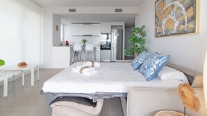 Una habitación de hotel moderna con una cama, un sofá, una mesa de comedor y una cocina al fondo.