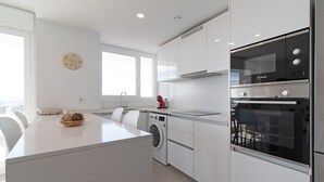 Cocina moderna con armarios blancos, horno Bosch, lavadora y un amplio ventanal que proporciona luz natural.