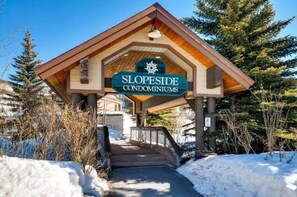 A wooden building with a sign reading "SLOPESIDE CONDOMINIUMS" and a snow-covered ground.