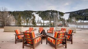 Eine Terrasse mit Sitzgelegenheiten im Freien und einem Feuerkorb, mit Blick auf eine verschneite Berglandschaft.
