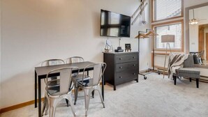 Ein modernes Wohnzimmer mit Esstisch, Stühlen, Fernseher, Kommode und Sofa.