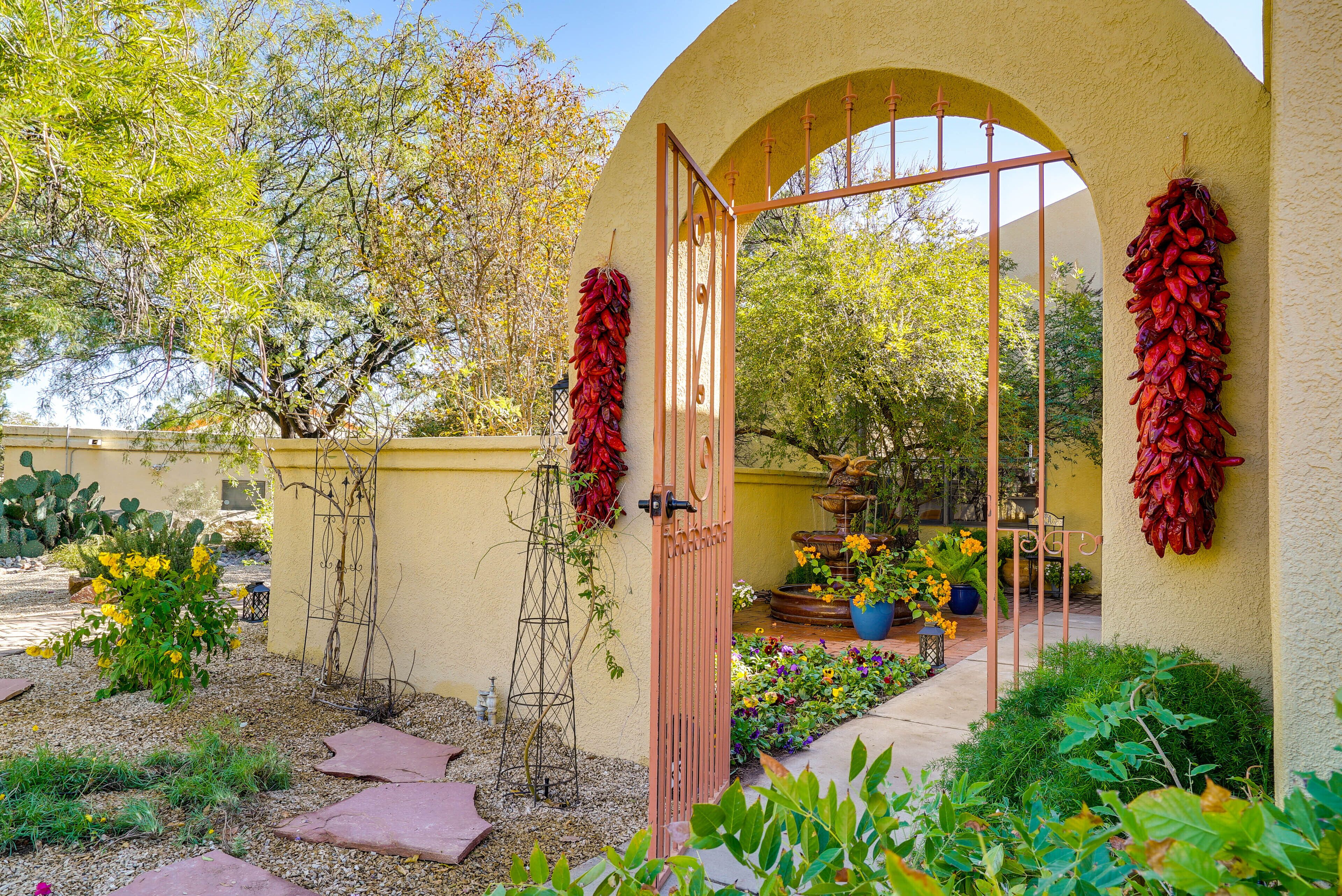 Un giardino con un muro giallo, un cancello in legno e peperoncini rossi appesi.