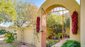 Un jardín con un muro amarillo, una verja de madera y pimientos rojos colgando.
