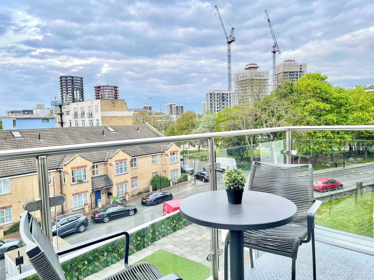 A balcony with a table and chairs, overlooking a residential street with cars and houses.