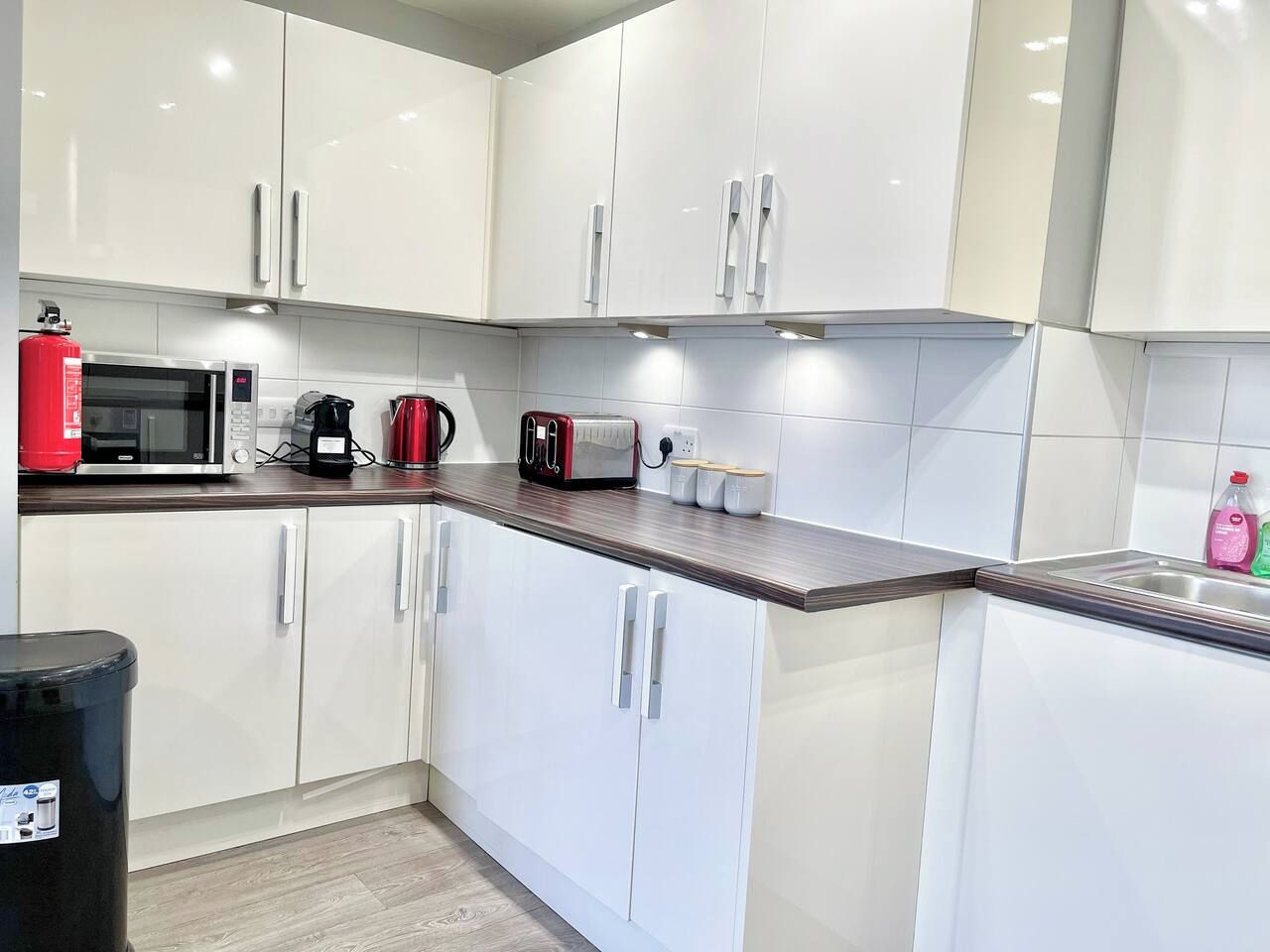 Een moderne keuken met witte kasten, een magnetron, een koffiezetapparaat en een broodrooster.