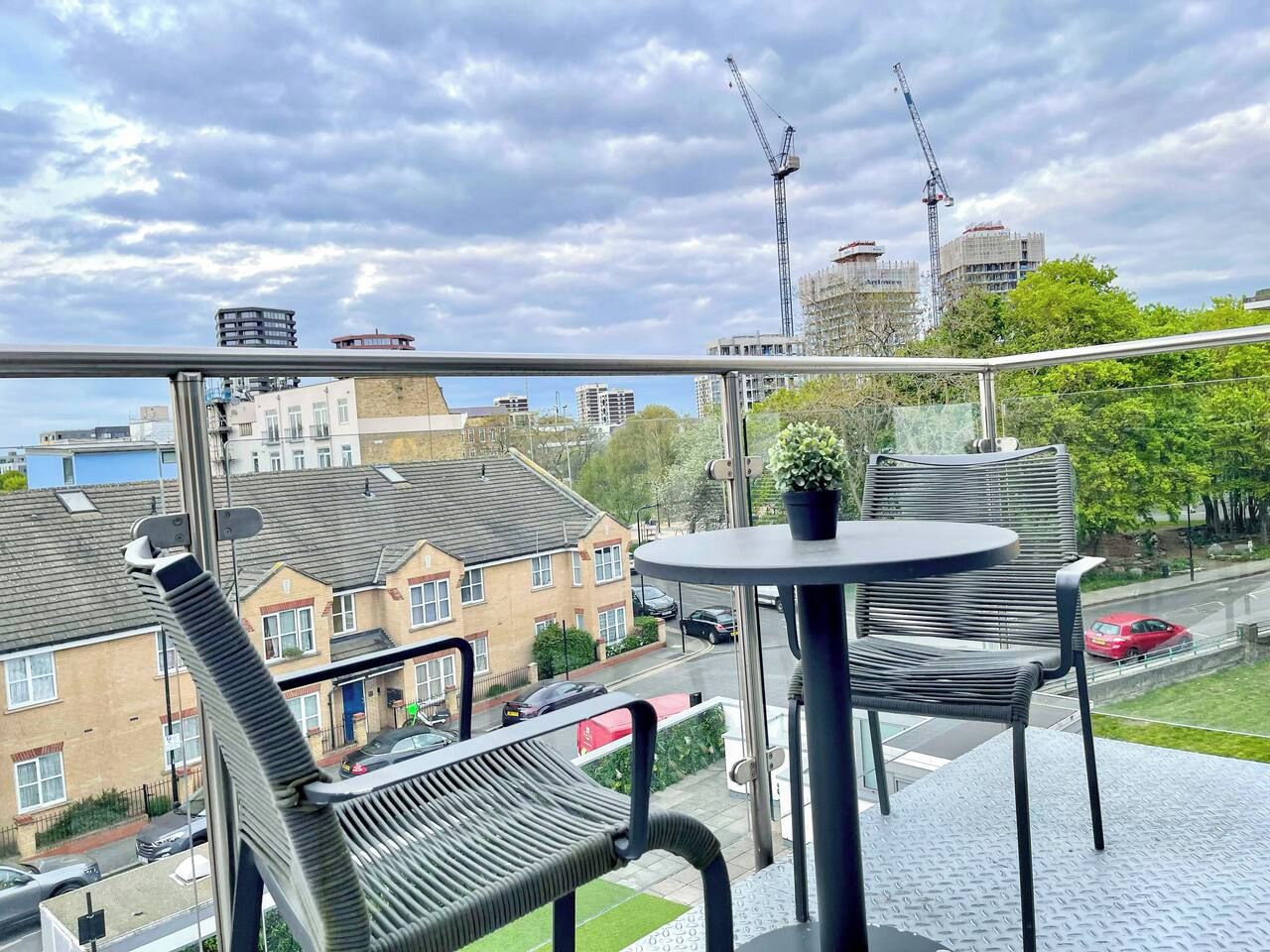 A balcony with a table and chairs, overlooking a residential area with houses and construction cranes.