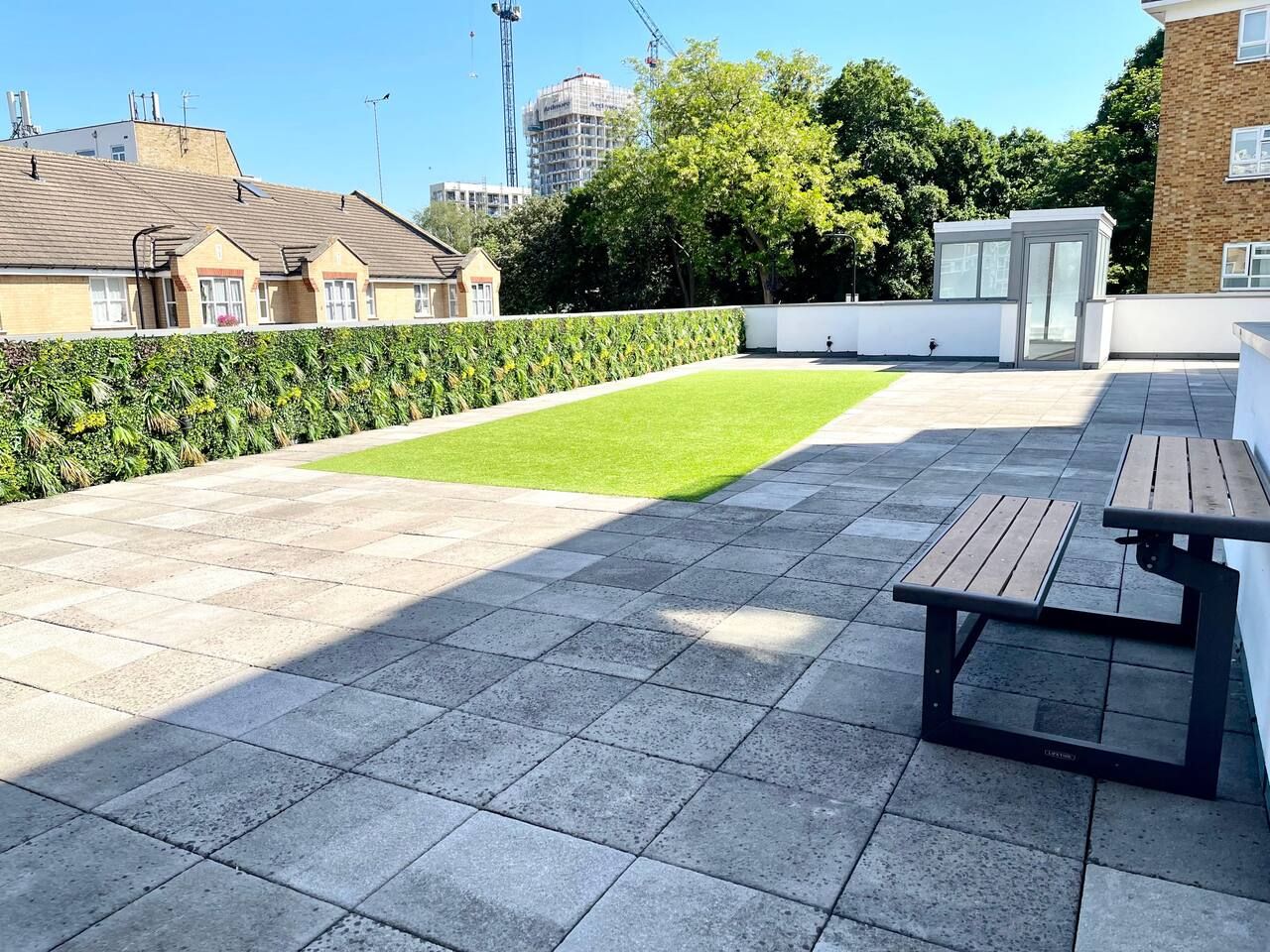 A rooftop terrace with a paved floor, a small lawn area, and a wooden table.