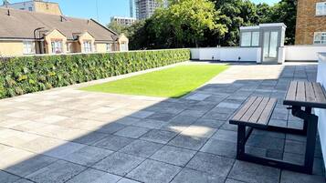 A rooftop terrace with a paved floor, a small lawn area, and a wooden table.
