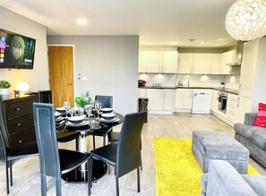 A modern living room with a dining area, a kitchen, and a TV mounted on the wall.