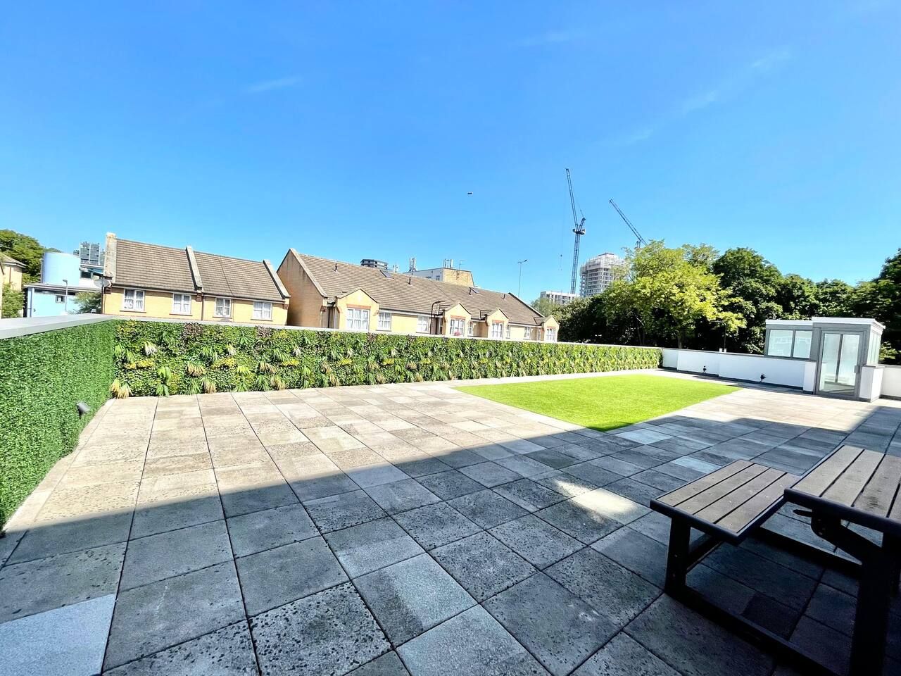 A courtyard with a paved patio, a wooden bench, and a well-maintained lawn.