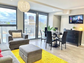 A modern living room with a sofa, ottoman, dining table, chairs, and a TV mounted on the wall.