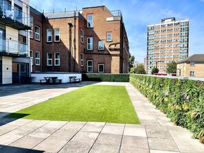 A courtyard with a green lawn, a seating area, and a building with multiple windows and balconies.