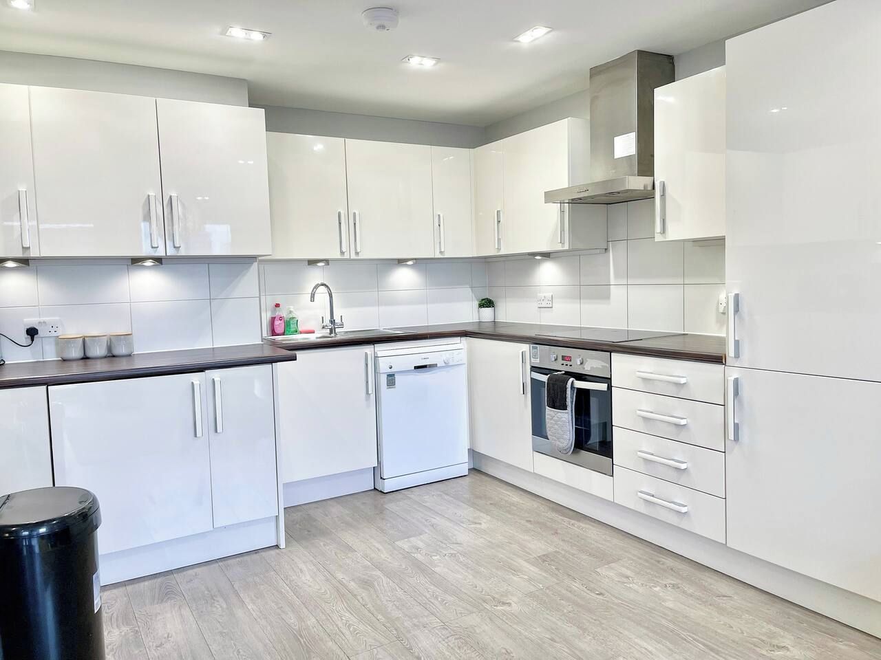 A modern kitchen with white cabinetry, a dishwasher, an oven, and a sink.