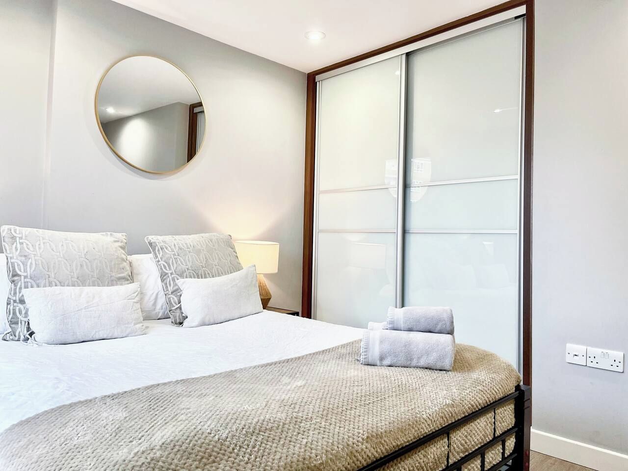 Een hotelkamer met een bed, kussens, een ronde spiegel, een bedlamp en een groot raam met gezandstraald glas.