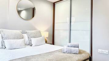 Een hotelkamer met een bed, kussens, een ronde spiegel, een bedlamp en een groot raam met gezandstraald glas.