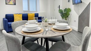 Een moderne eethoek met een ronde tafel voor vier personen, omringd door grijze gestoffeerde stoelen.