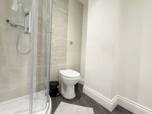 Une salle de bain avec une douche à parois de verre, des toilettes blanches et une poubelle noire.