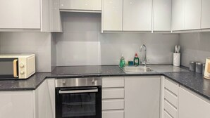 Cocina moderna con armarios blancos, horno empotrado, microondas y lavabo con grifo.