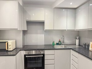 A modern kitchen with white cabinets, a built-in oven, a microwave, and a sink with a faucet.