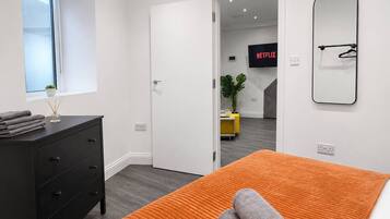 Ein modernes Schlafzimmer mit Bett, Kommode, Fenster und einer Tür zu einem anderen Raum.