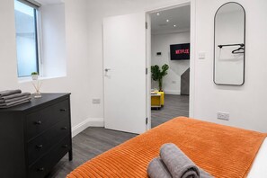 Une chambre à coucher moderne, avec un lit, une commode, une fenêtre et une porte donnant sur une autre pièce.