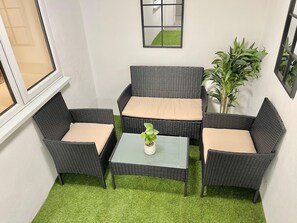 Un rincón con asientos de mimbre y una mesa de vidrio, con una pequeña planta en maceta.