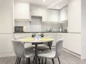 A modern kitchen with white cabinets, a round dining table with chairs, and a microwave.
