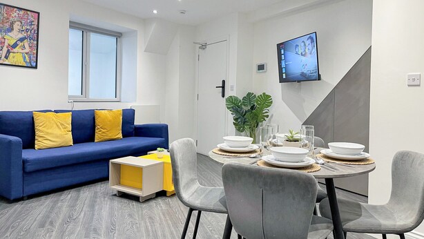 Een moderne woonkamer met een blauwe bank, een eettafel met witte borden en glazen, en een groot raam.