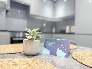A modern kitchen with a potted plant and a thank you card on the counter.