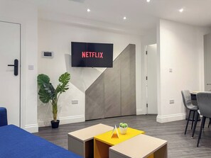 A modern office space with a flat-screen TV displaying 'NETFLIX' in red letters, a potted plant, and a small table with a yellow top.