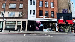 Straatbeeld met een combinatie van bedrijfsgebouwen, waaronder een winkel genaamd 'Fixhere' en een restaurant genaamd 'Ah...'.