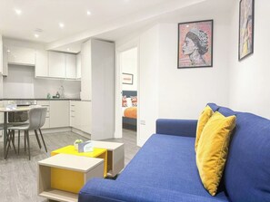 A modern living room with a blue sofa, a yellow coffee table, and a dining area with a chair and table. - Old St 1-bed Flat W/ patio near hoxton, shoreditch (London)