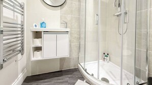 Un baño moderno con ducha envuelta en vidrio, un tocador blanco con espejo y un perchero.