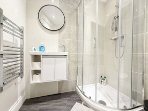 A modern bathroom with a glass-enclosed shower, a white vanity with a mirror, and a towel rack.
