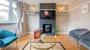 Una sala de estar con chimenea, dos sofás, una mesa de centro y un televisor sobre la chimenea.