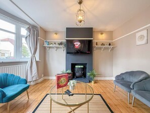 Una sala de estar con chimenea, dos sofás, una mesa de centro y un televisor sobre la chimenea.
